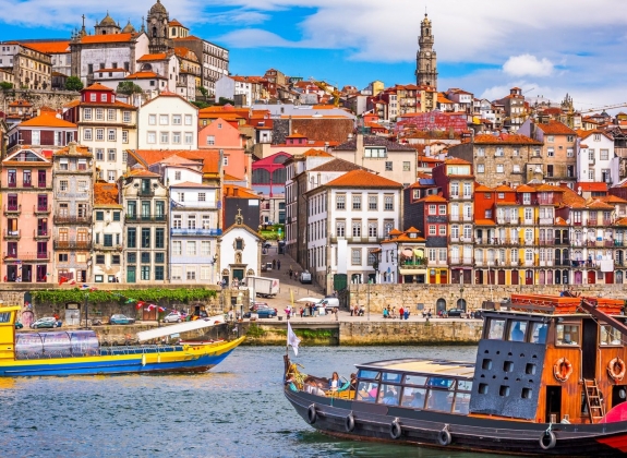 Wooden tour boats cruise the river in Porto, Portugal with the colorful city skyline in the background