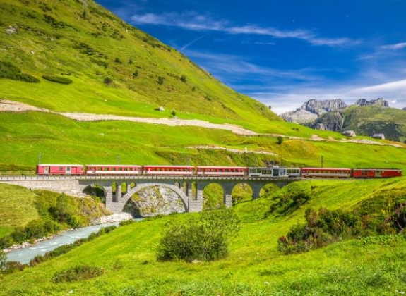 A train travels past green landscape with brilliant blue sky