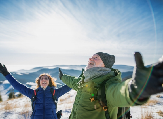 Senior couple hikers in snow-covered winter nature, stretching arms.