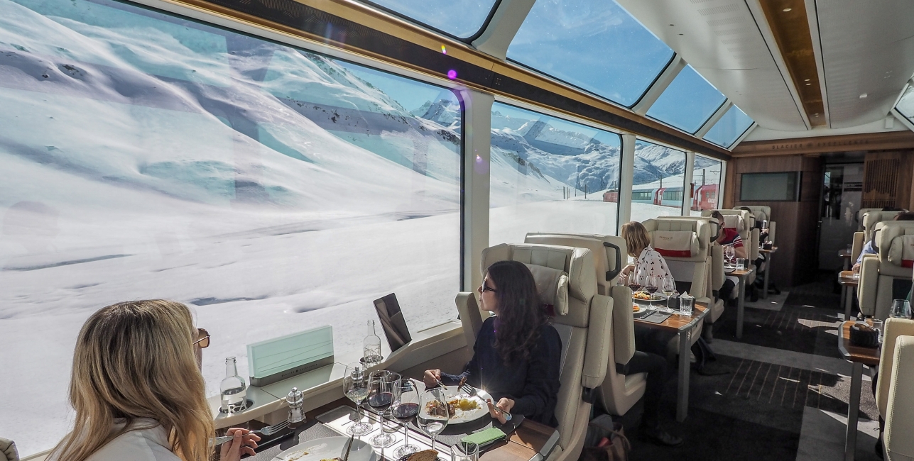 Onboard the Glacier Express - Excellence Class Train travellers look out of the window and the snowy Alpine scenery