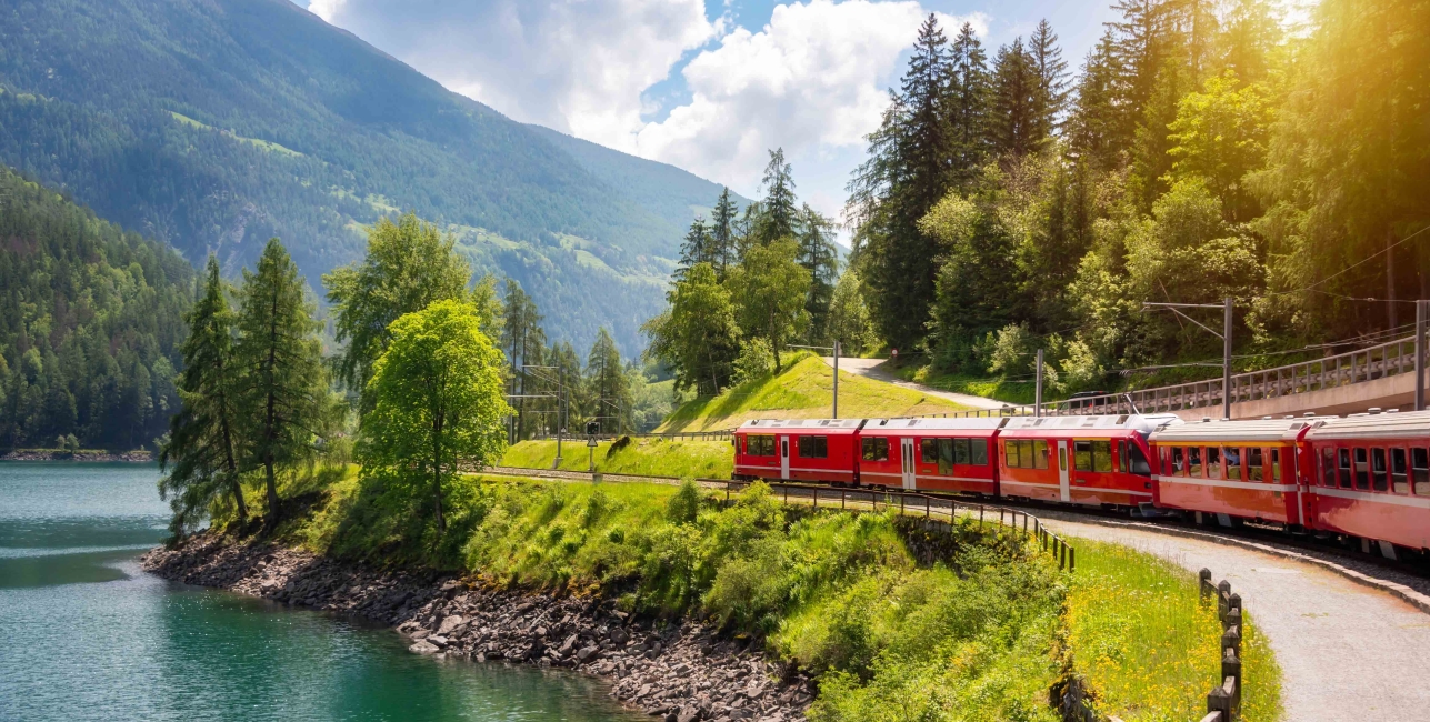 Red train moving along lake in beautiful mountain landscape in Switzerland