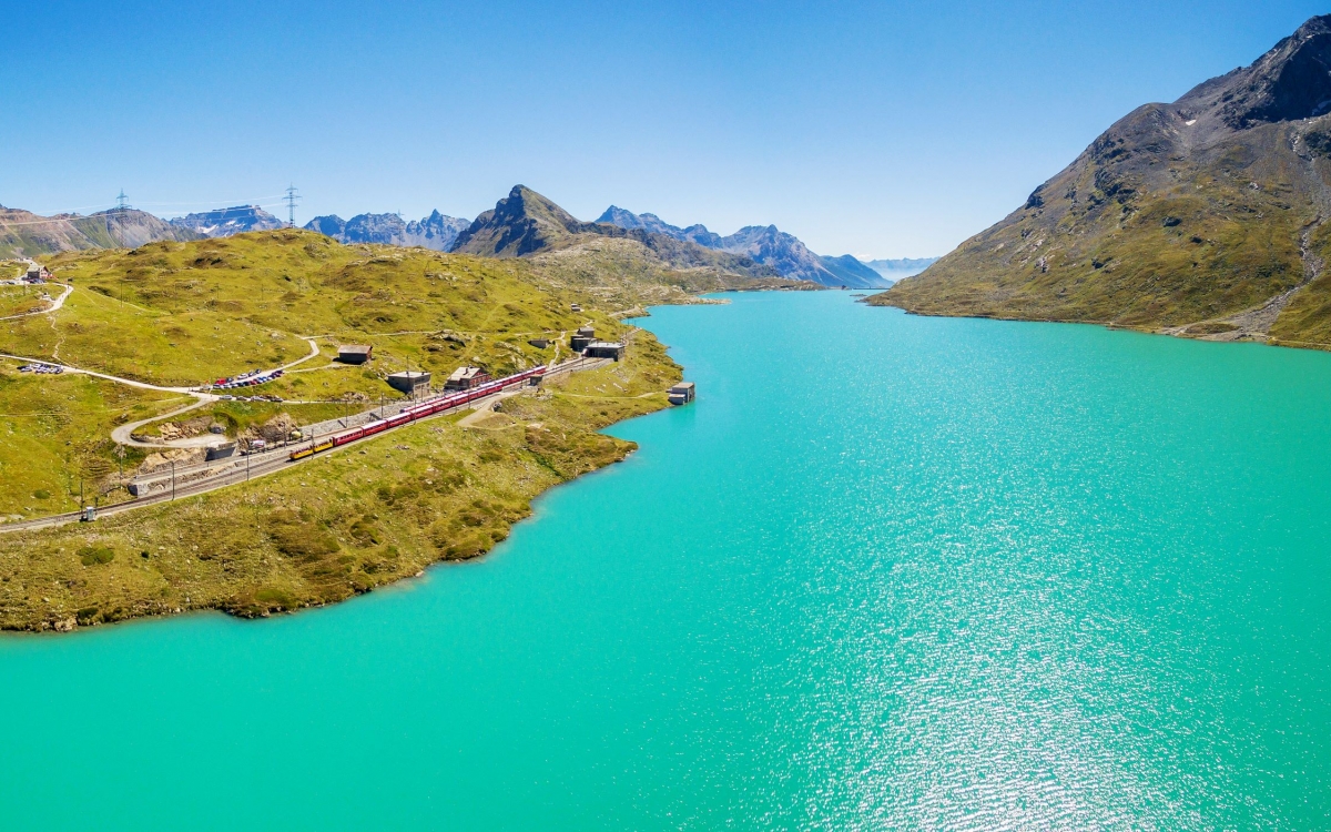 The Bernina Express at the Bernina Pass A train travels alongside a vast turquoise lake