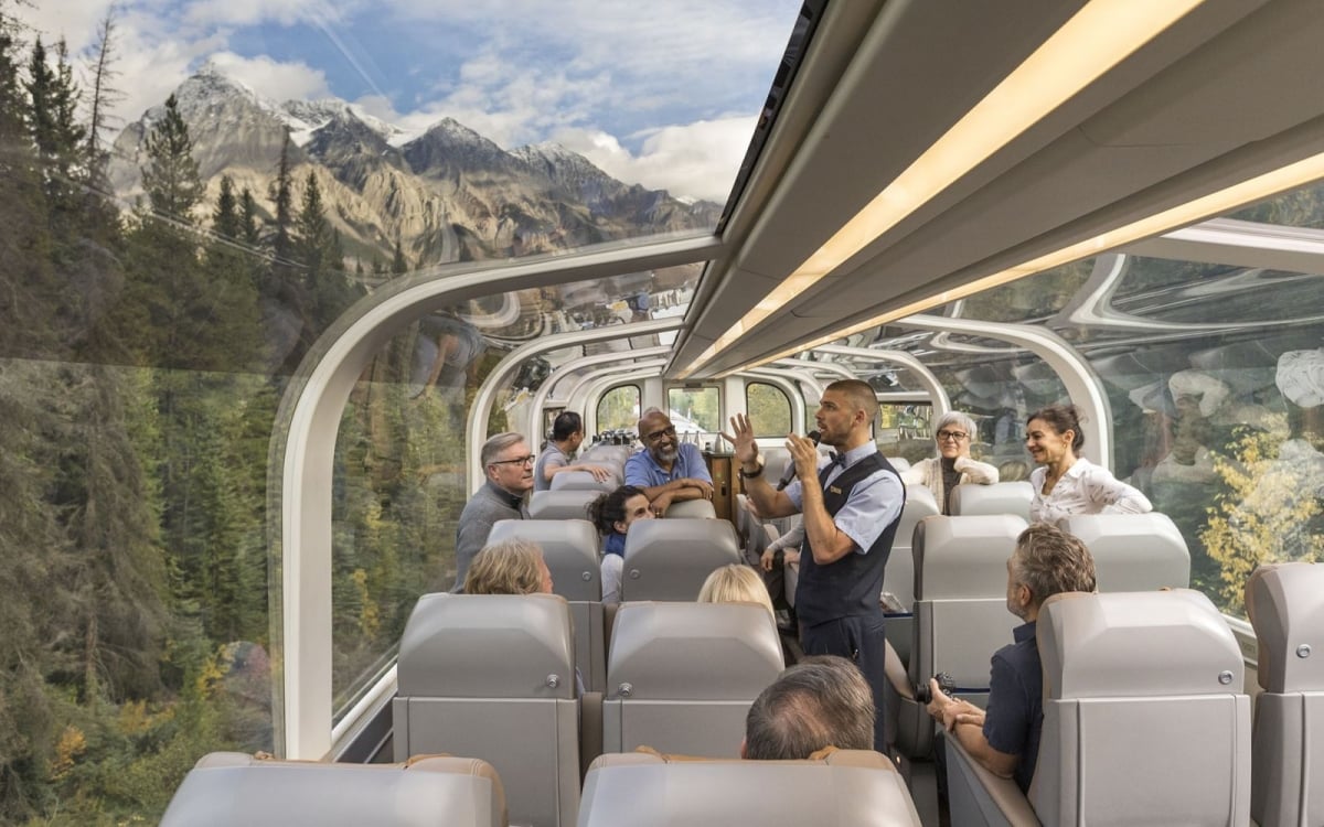 Train staff talk to animated passengers passing through mountain scenery