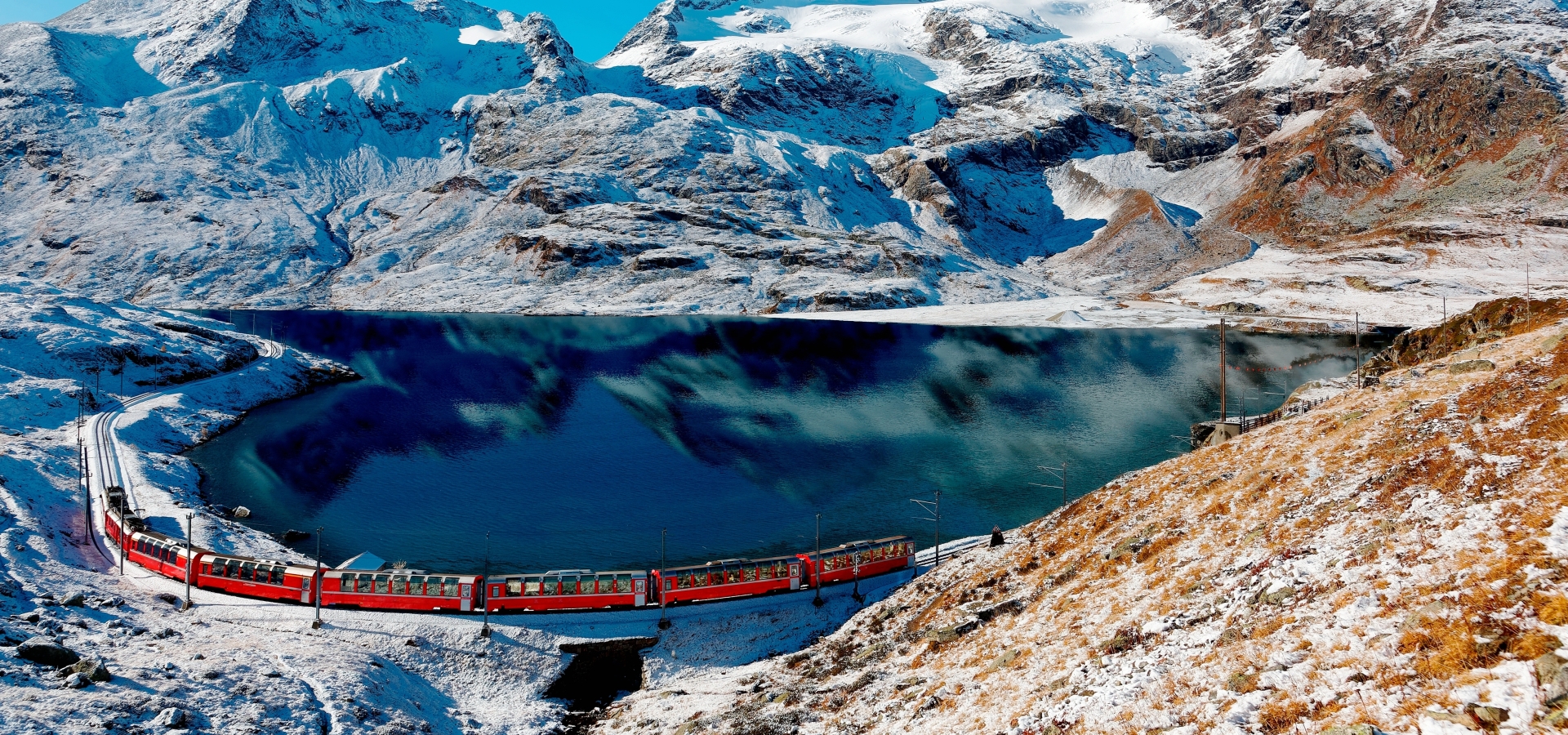 The Bernina Express at the Bernina Pass A train travels alongside a bright blue lake in winter