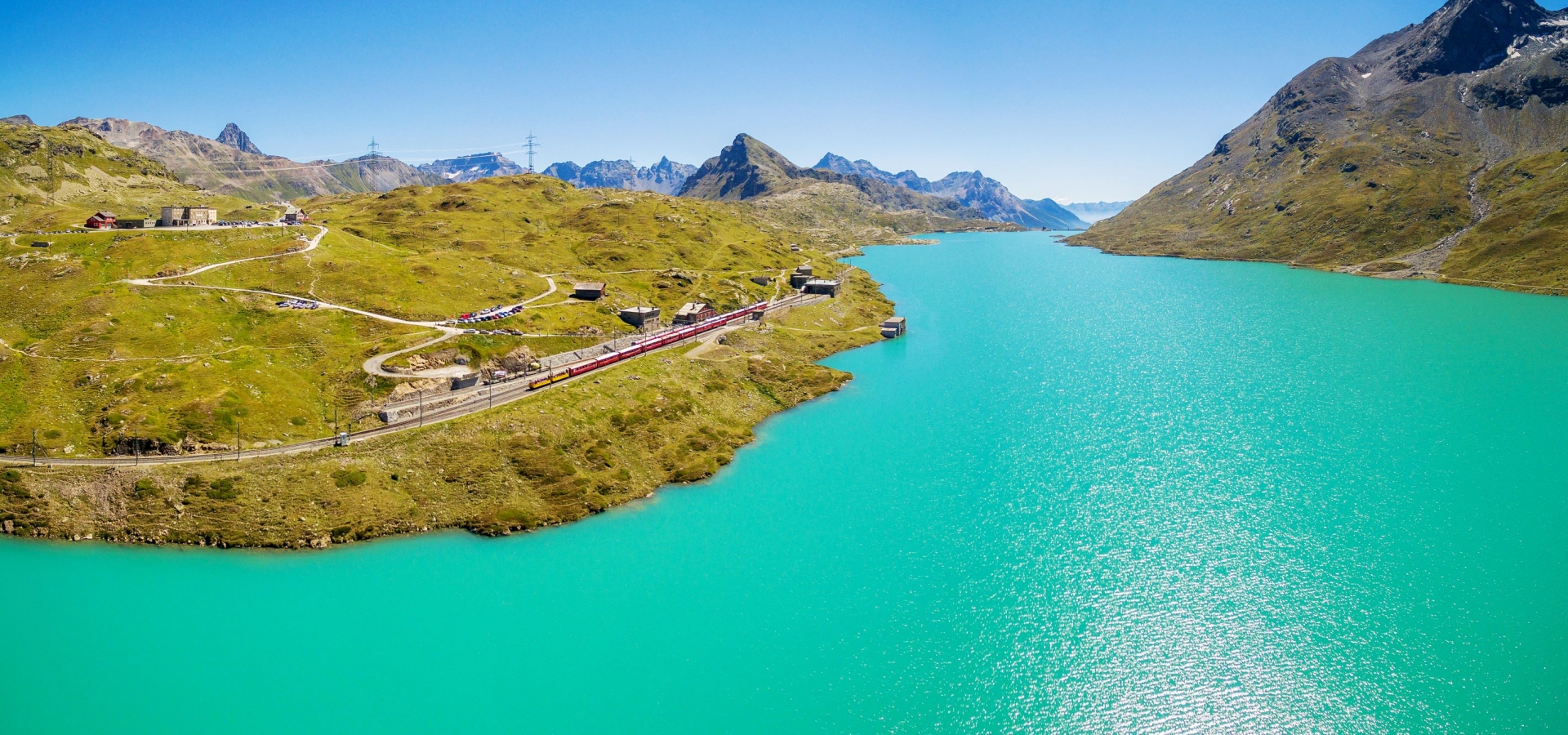 The Bernina Express at the Bernina Pass A train travels alongside a vast turquoise lake