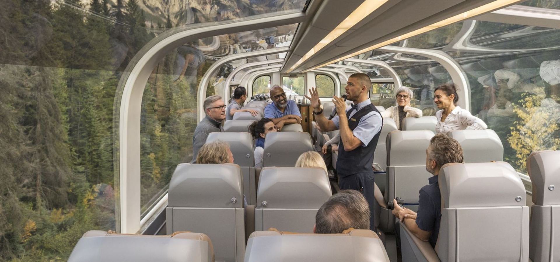Train staff talk to animated passengers passing through mountain scenery