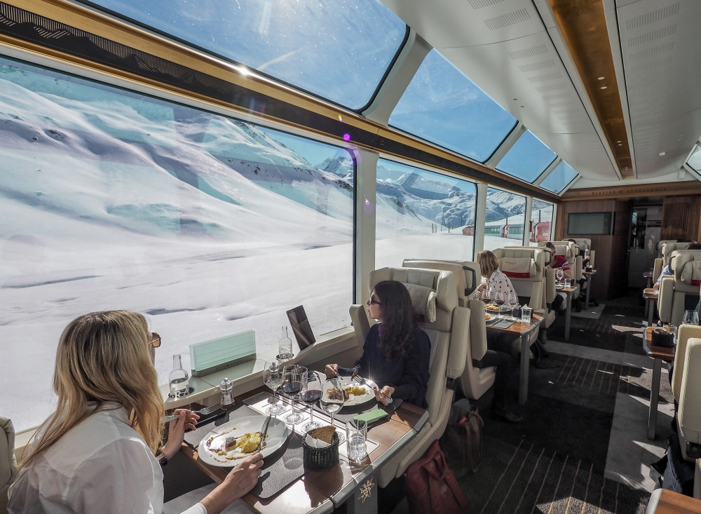 Onboard the Glacier Express - Excellence Class Train travellers look out of the window and the snowy Alpine scenery